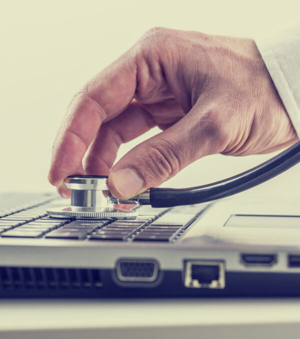 Man checking his laptop computer with a stethoscope holding the disk over the keyboard as he looks for viruses and malware, toned retro or instagram effect.